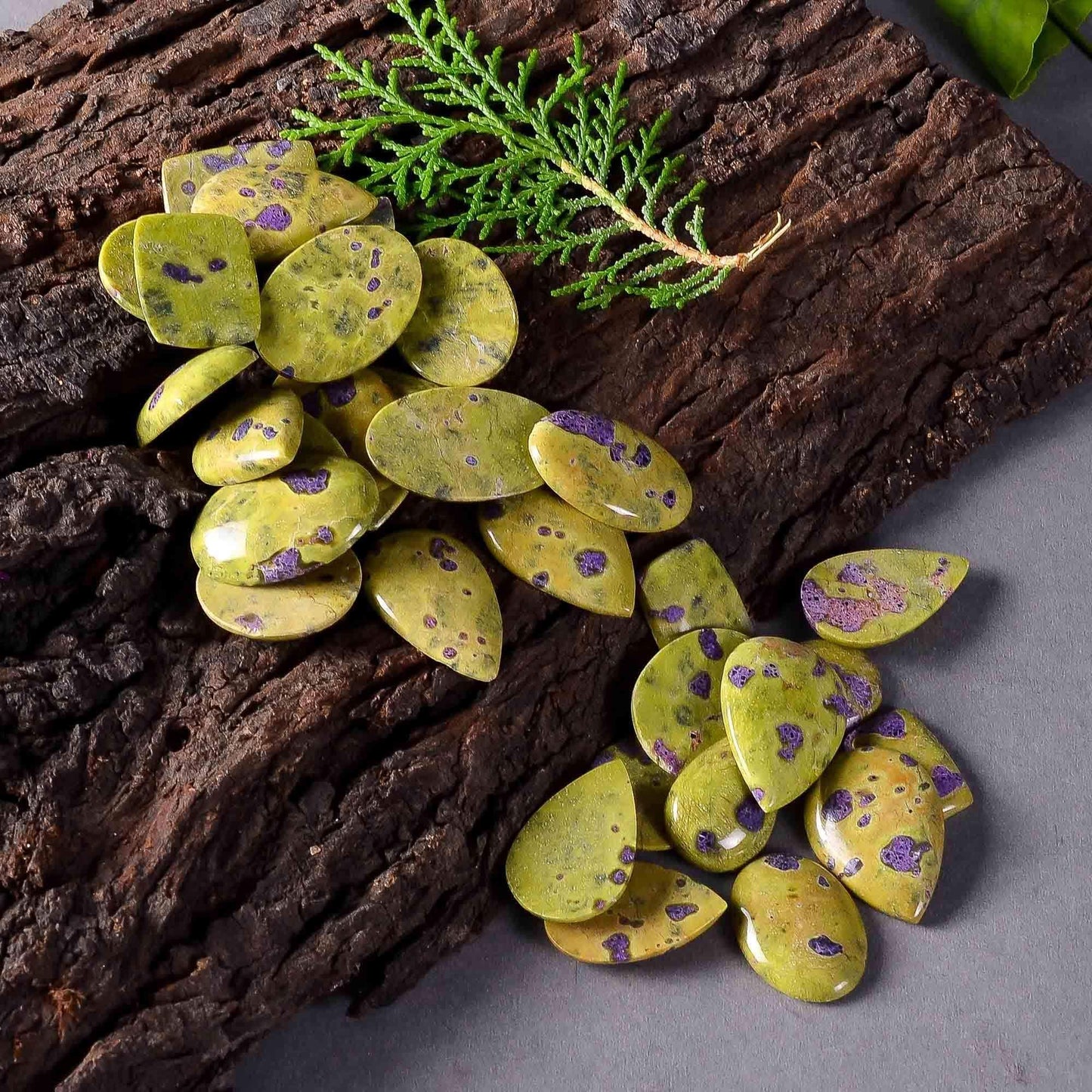 Green and purple speckled stones on a wooden surface with a branch