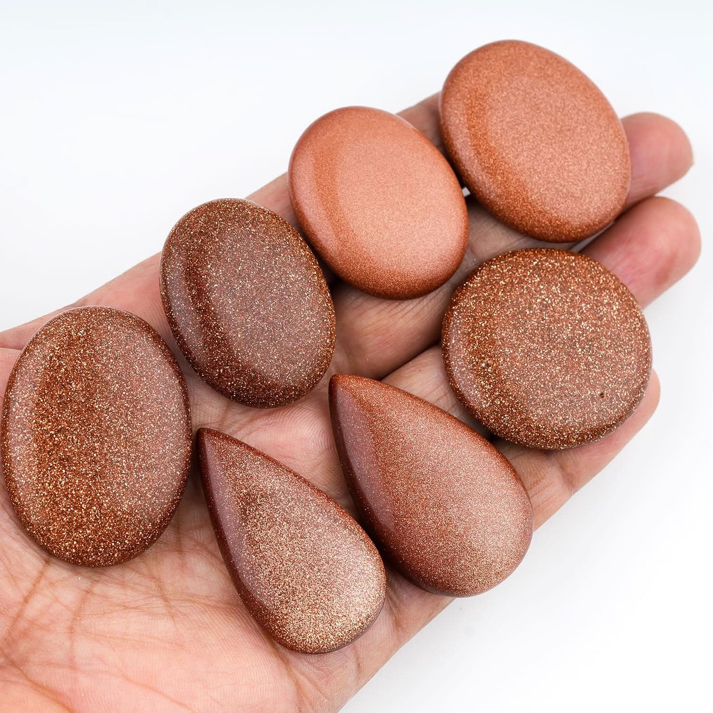 sunstone for jewelry makin, Hand holding a collection of brown stones against a white background