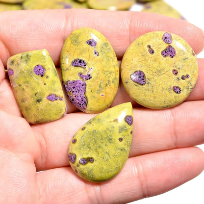 Four yellow stones with purple and black speckles held in a hand.