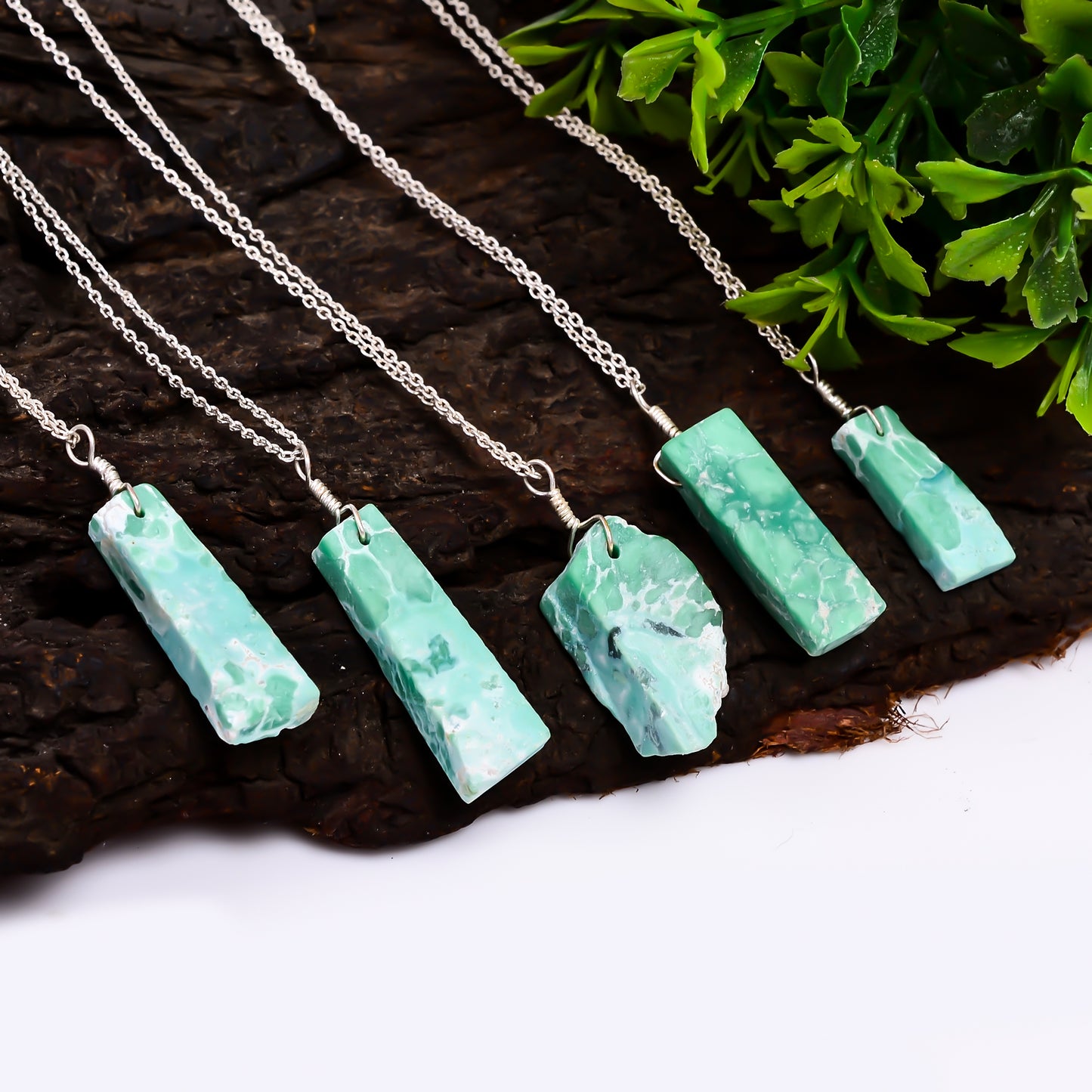 Raw variscite gemstone pendant necklaces arranged outdoors on a natural background showing green hues and irregular bar shapes
