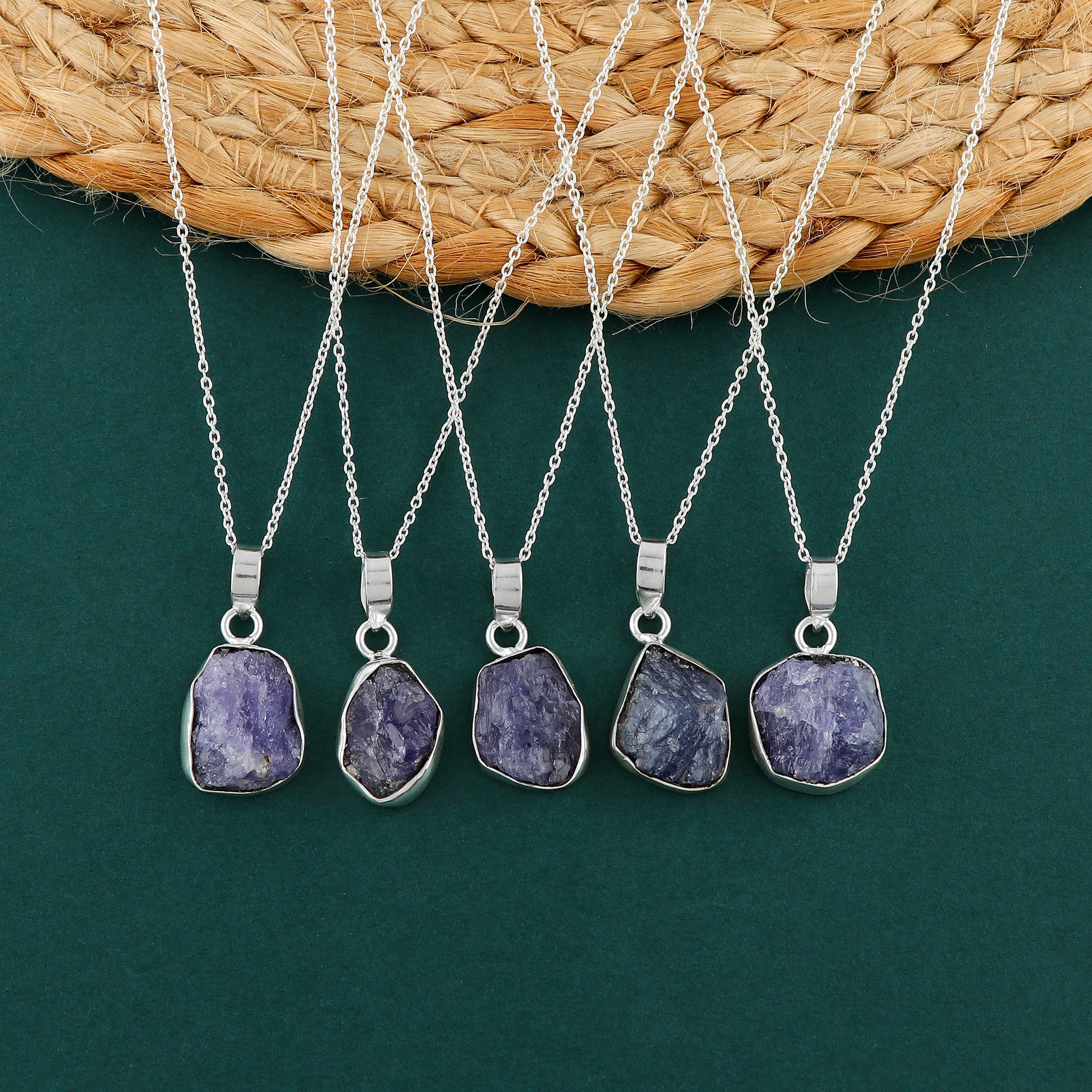 Real tanzanite raw stone pendant held in hand showing natural blue color, bezel frame and silver-plated chain details