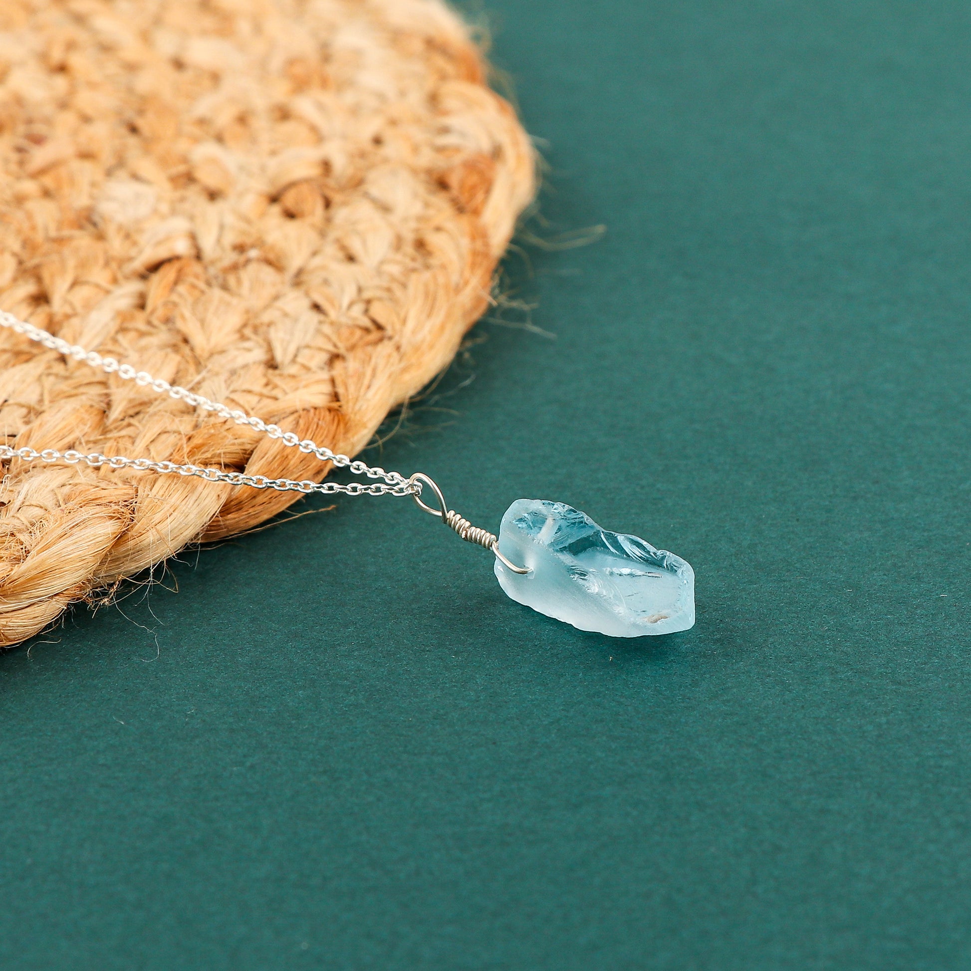 Raw sky blue topaz gemstone pendant displayed against a white background with silver-plated chain and natural rough cut