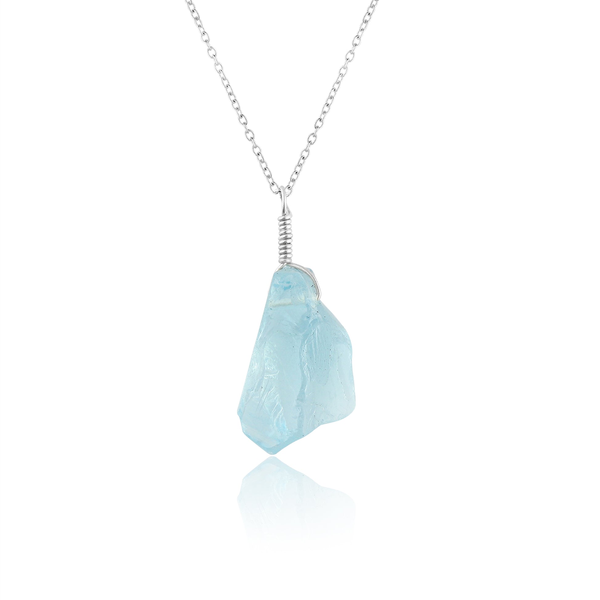 Sky blue topaz raw gemstone pendant held in hand showing natural rough cut and vibrant blue color on silver-plated chain