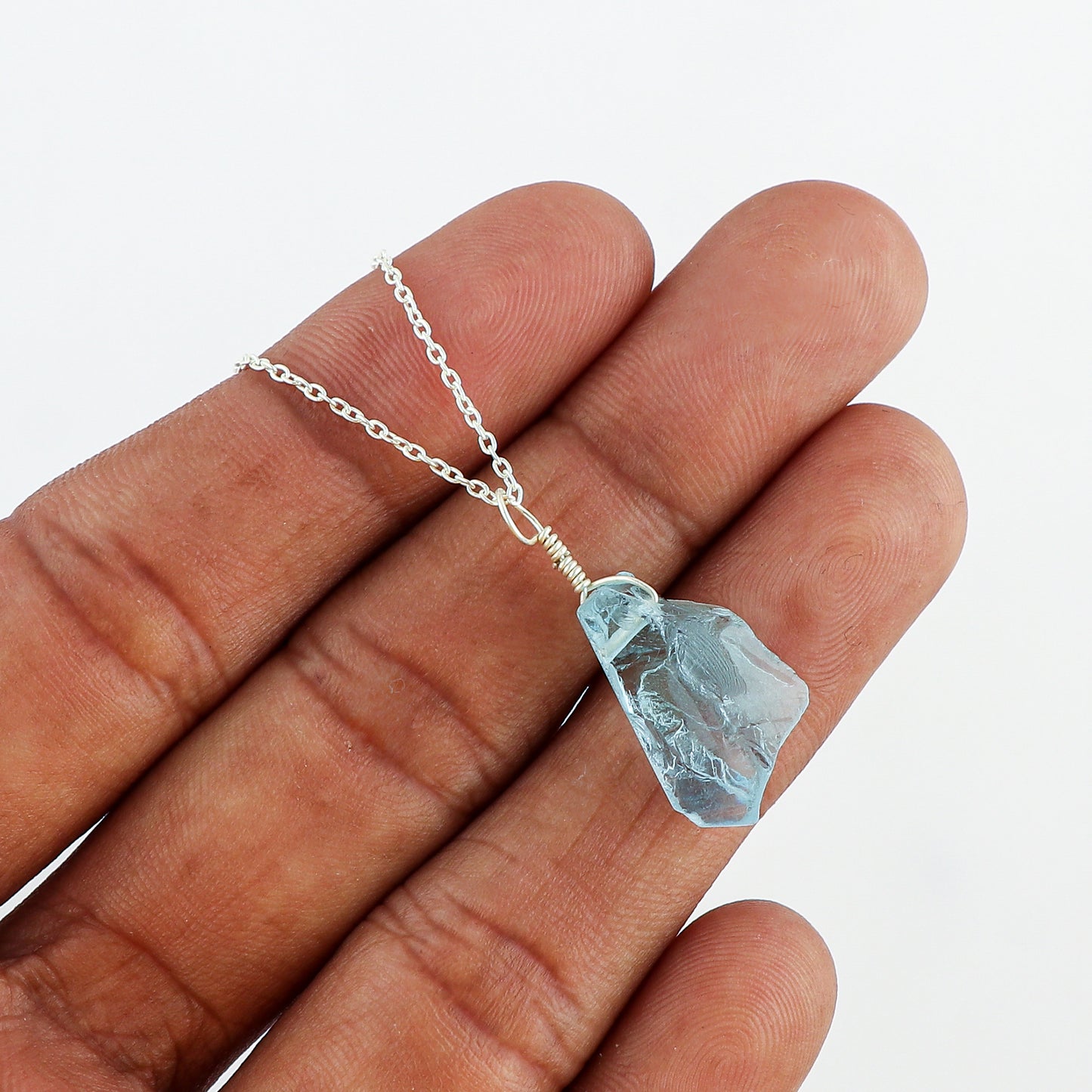 Close-up of natural sky blue topaz raw crystal pendant showing rough texture, irregular shape and bright gemstone color