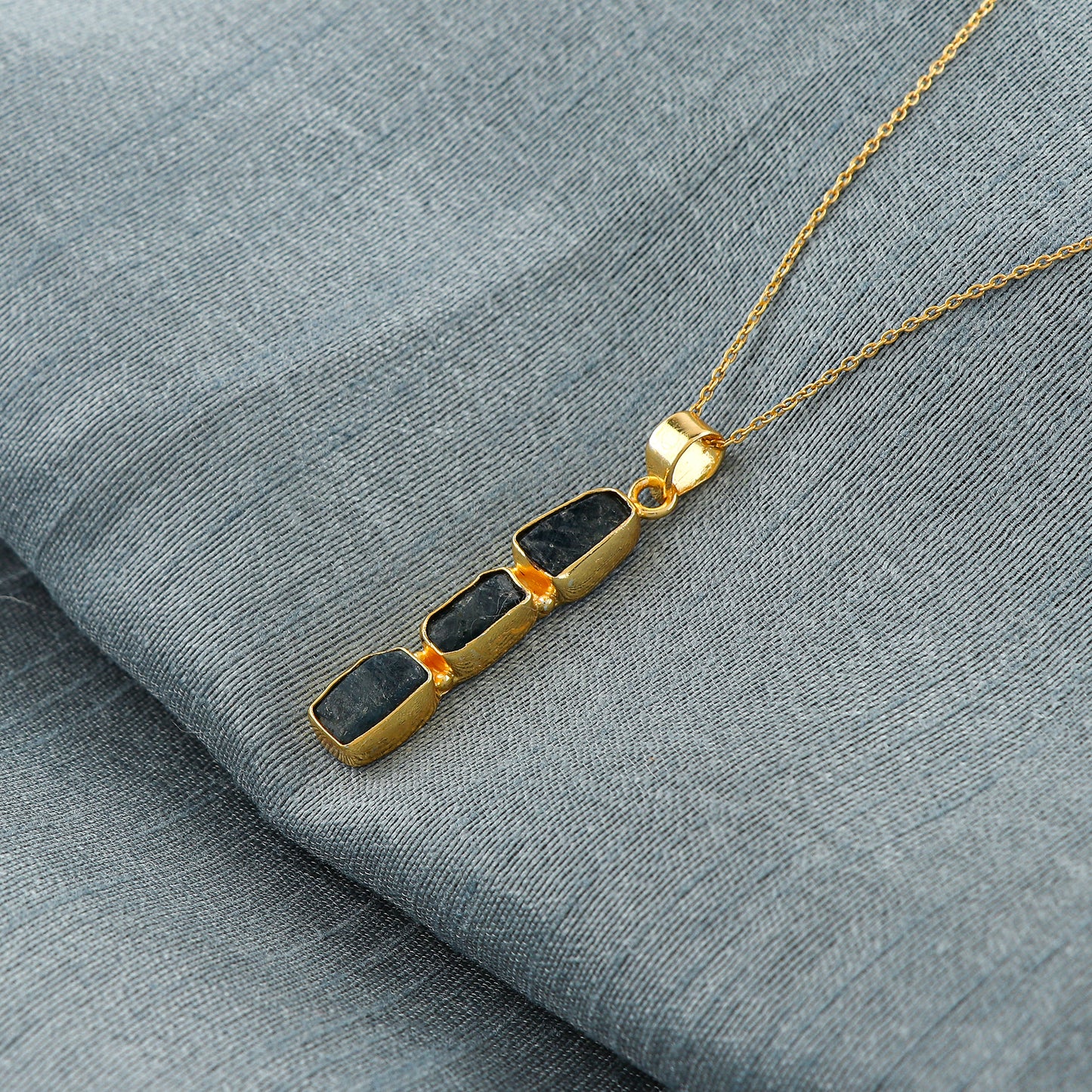 Close-up view of natural sapphire raw gemstone pendant with irregular cut set in gold bezel on 18-inch chain
