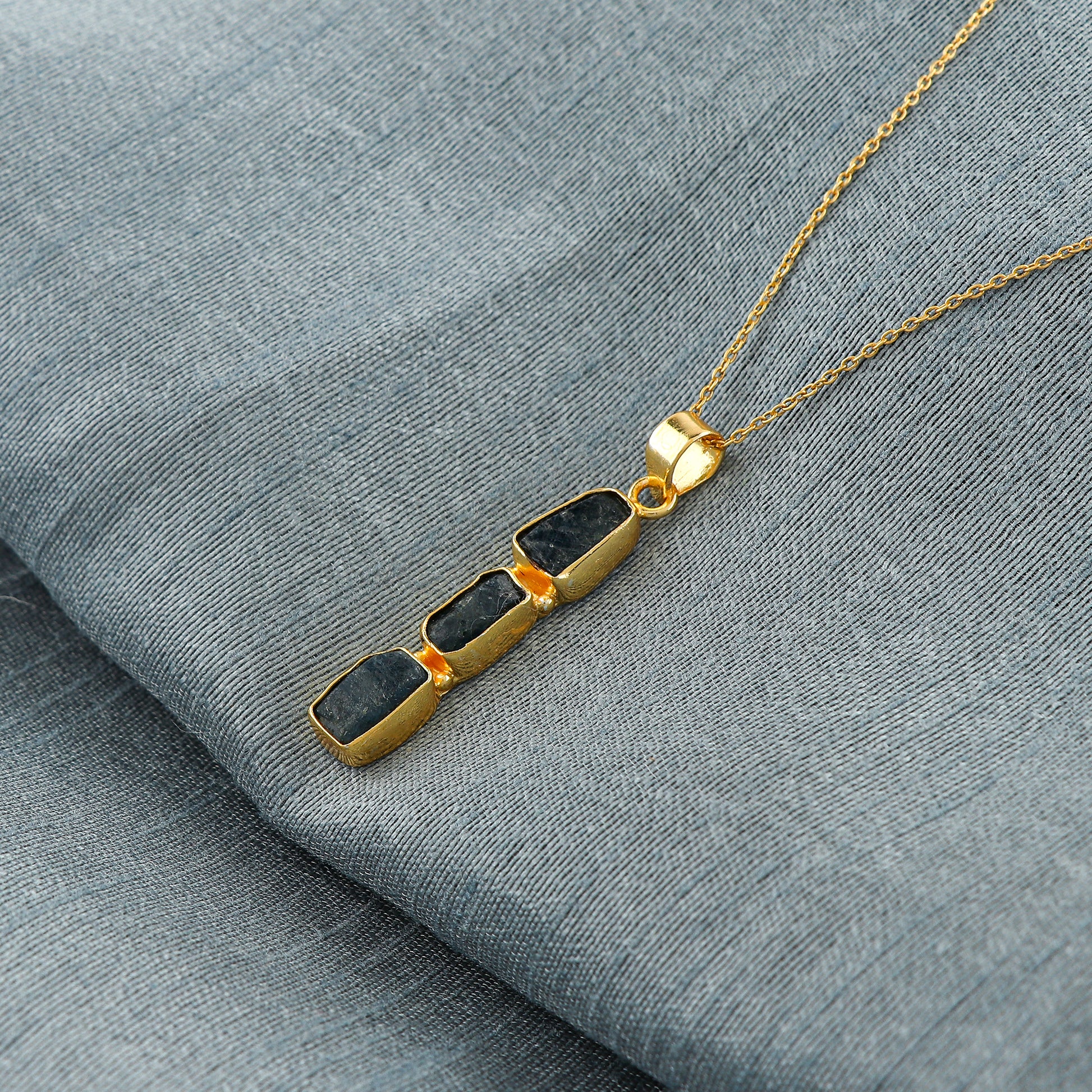 Close-up view of natural sapphire raw gemstone pendant with irregular cut set in gold bezel on 18-inch chain