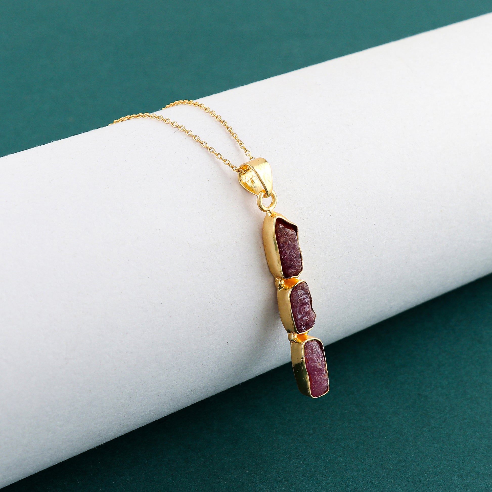 Close-up of natural ruby raw gemstone pendant with irregular cut set in gold bezel on a delicate 18-inch chain