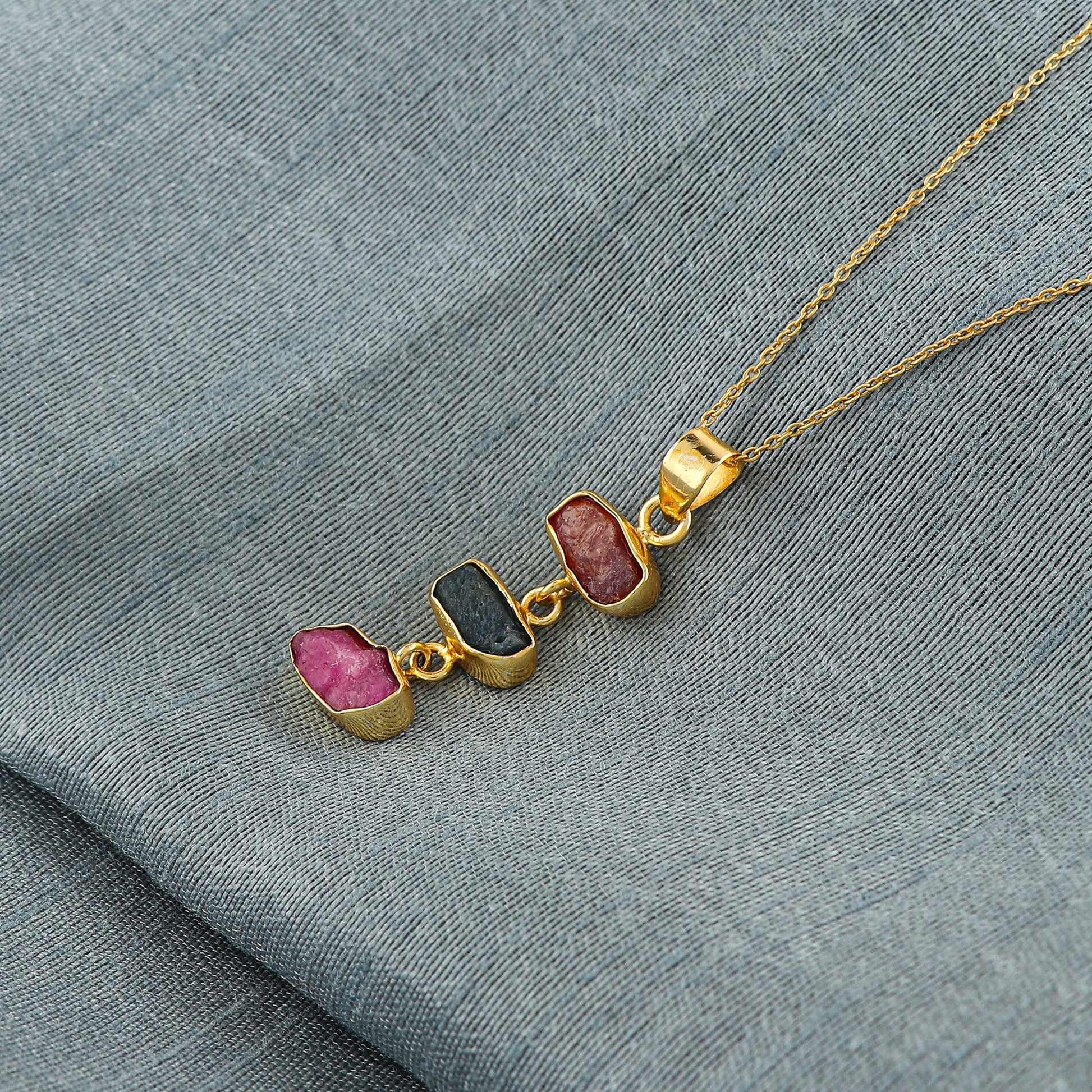 Natural sapphire and ruby raw crystal pendant necklaces arranged in a row with blue and pink stones in gold-plated bezels on 18-inch chain