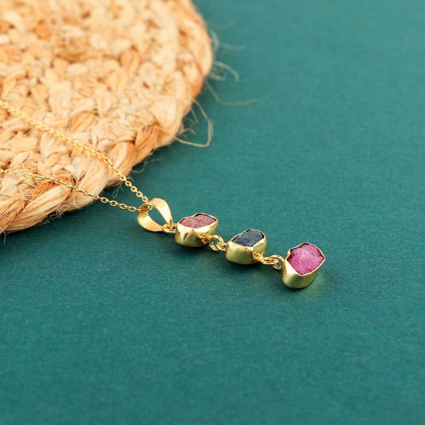 Dual gemstone sapphire and ruby raw crystal pendant necklace placed on soft fabric showing rich blue and pink colors with gold-plated setting