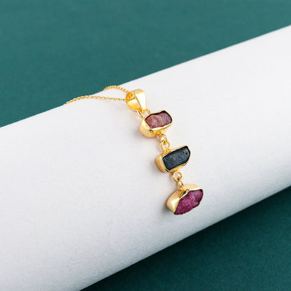 Close-up of natural sapphire and ruby raw gemstone pendant with irregular cuts set in gold-plated bezel on 18-inch chain