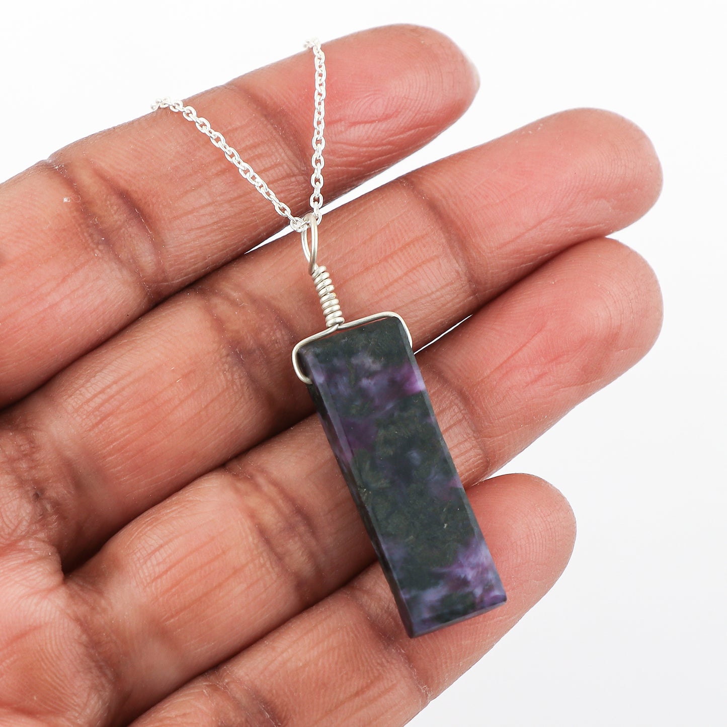 Hand holding a necklace with a rectangular pendant