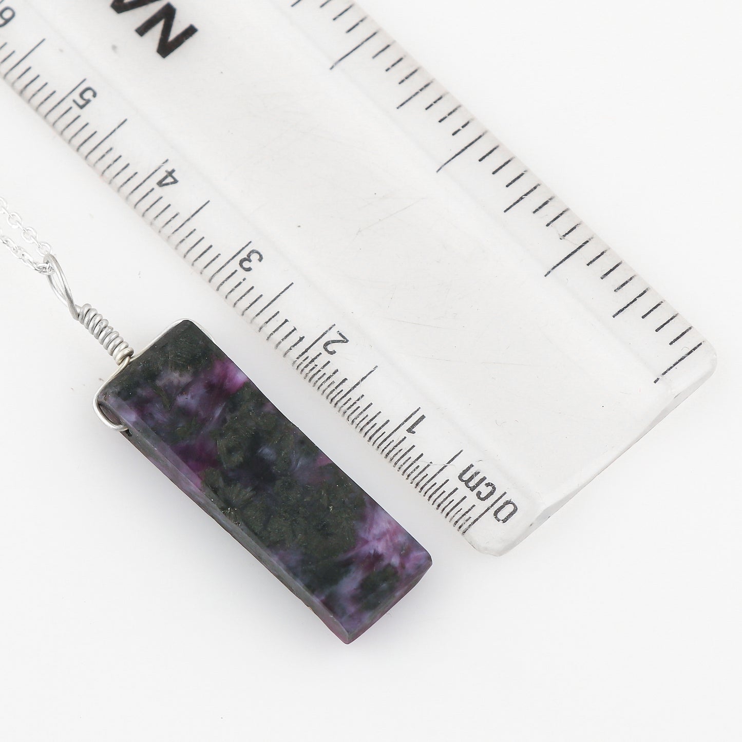 Rectangular purple and black patterned pendant with a ruler for scale on a white background