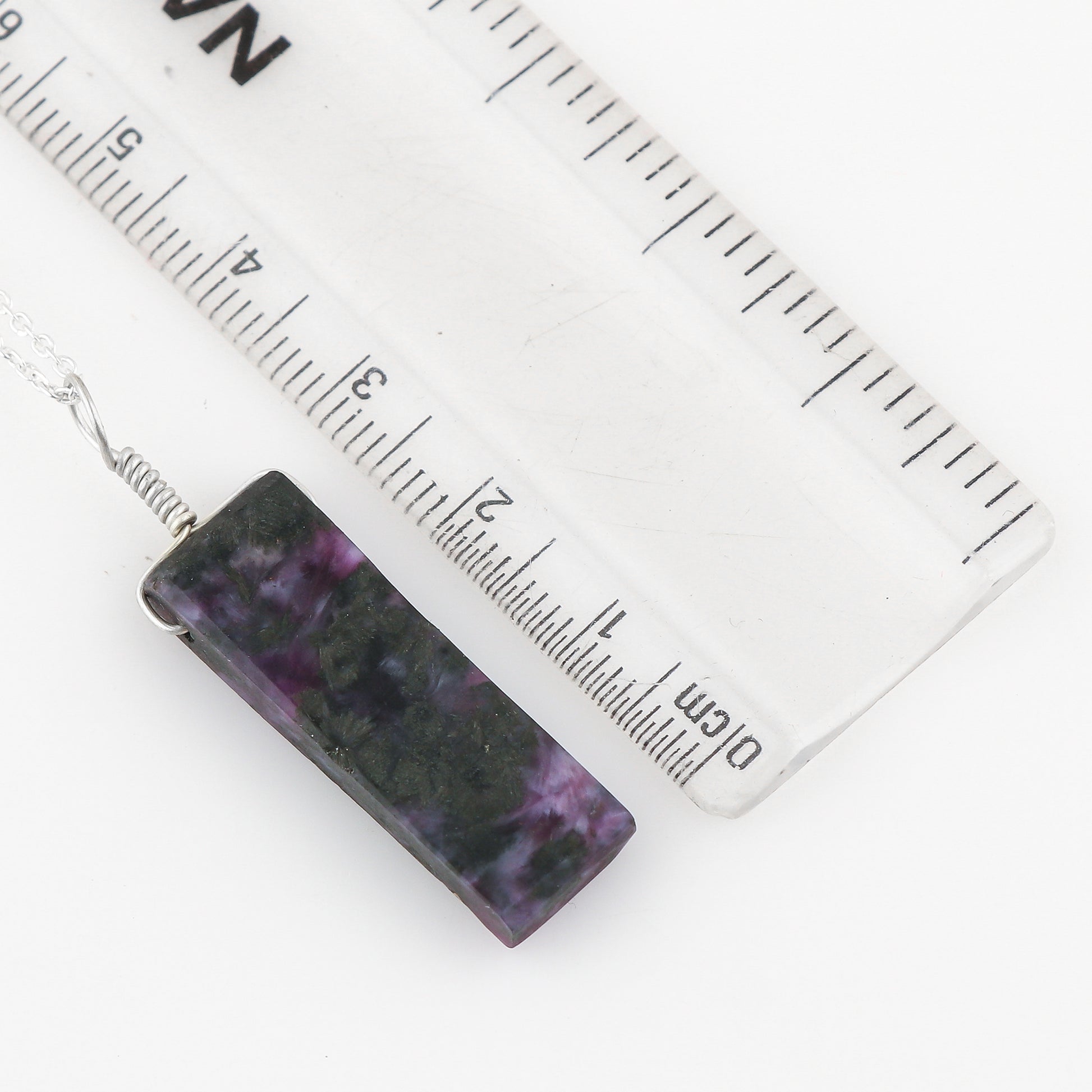 Rectangular purple and black patterned pendant with a ruler for scale on a white background