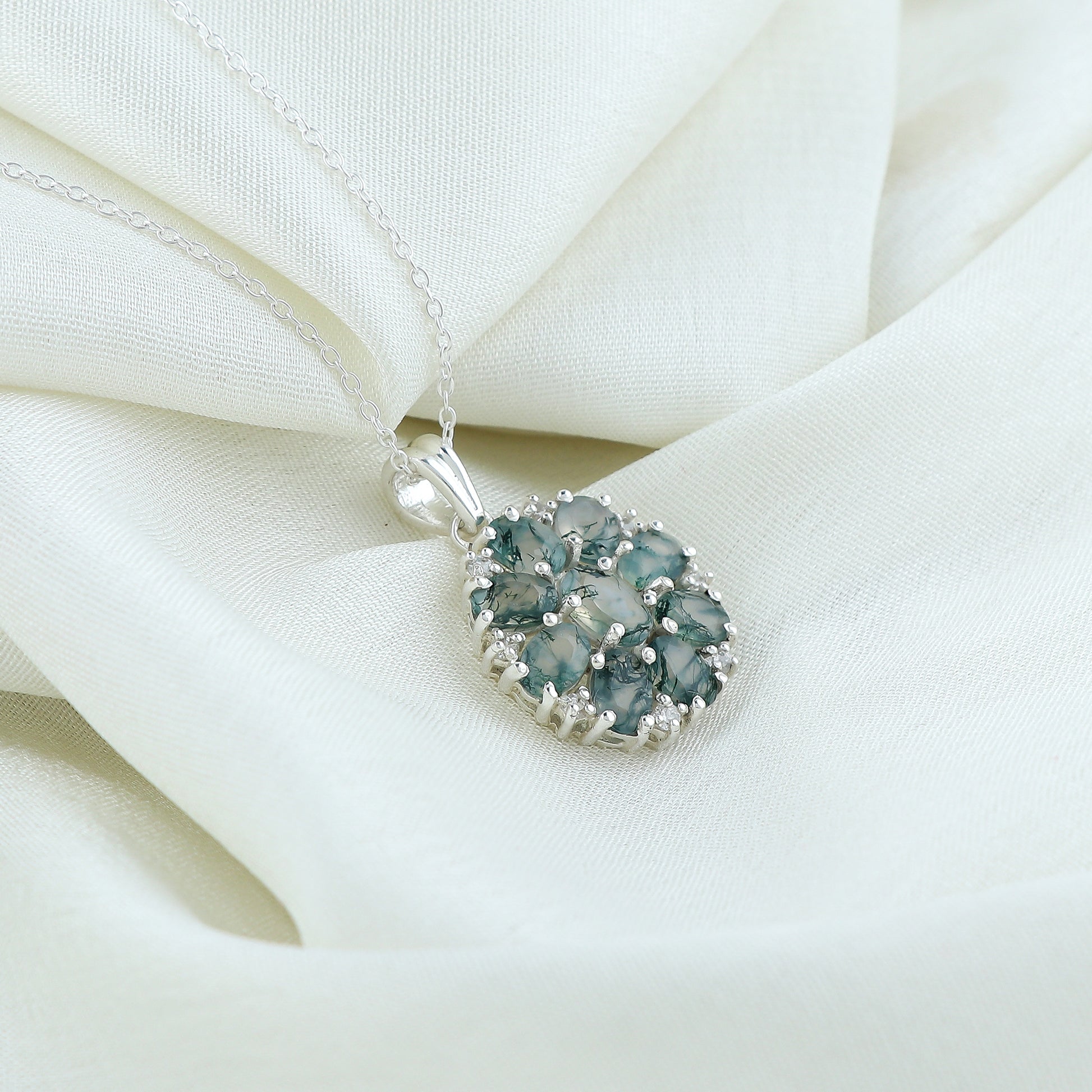 Silver necklace with a green gemstone pendant on a white fabric background