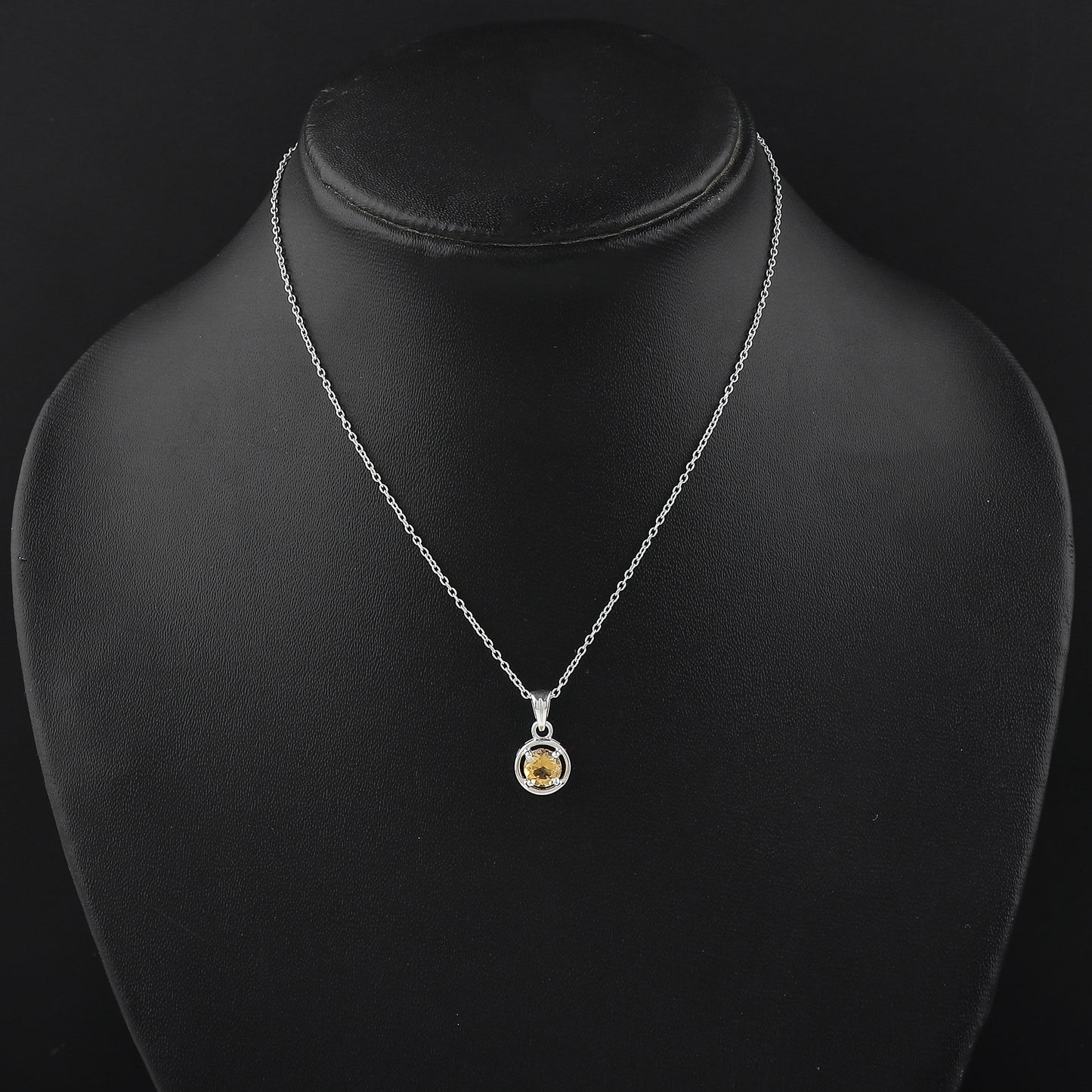 Silver necklace with a yellow gemstone pendant on a black mannequin.