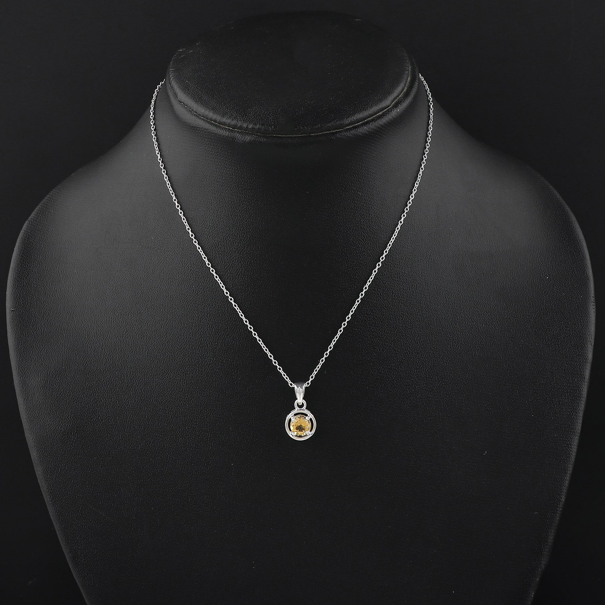 Silver necklace with a yellow gemstone pendant on a black mannequin.