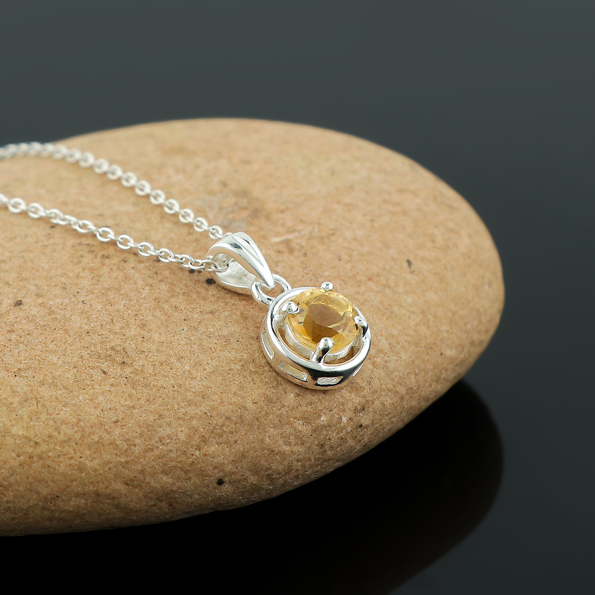 Silver necklace with a yellow gemstone pendant on a stone surface
