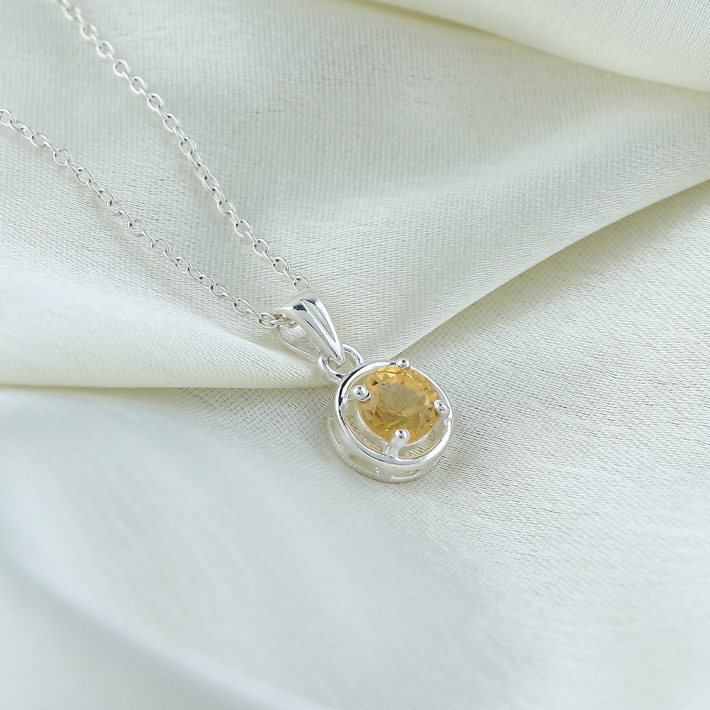Silver necklace with a yellow gemstone pendant on a white fabric background