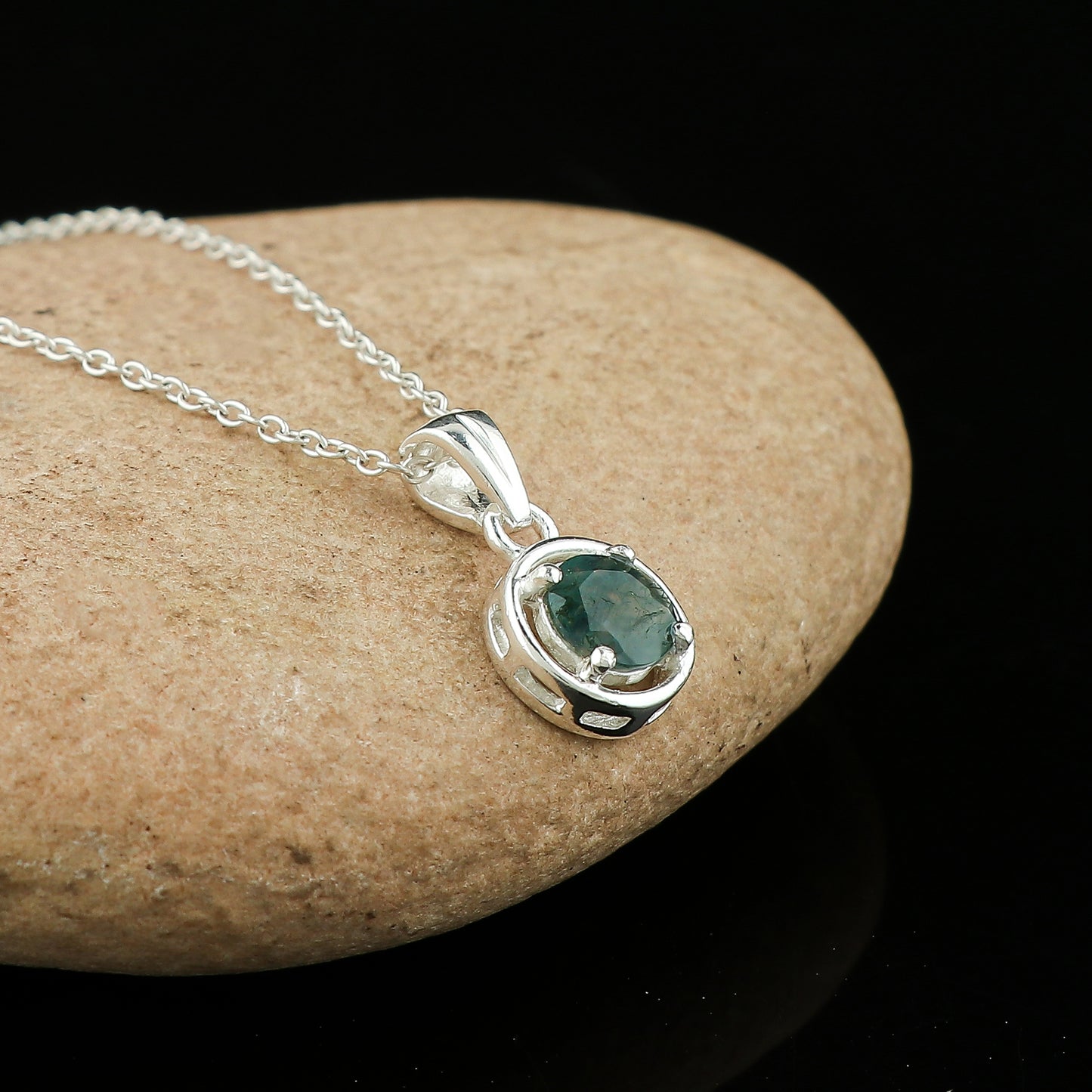 Silver pendant with a green gemstone on a stone surface