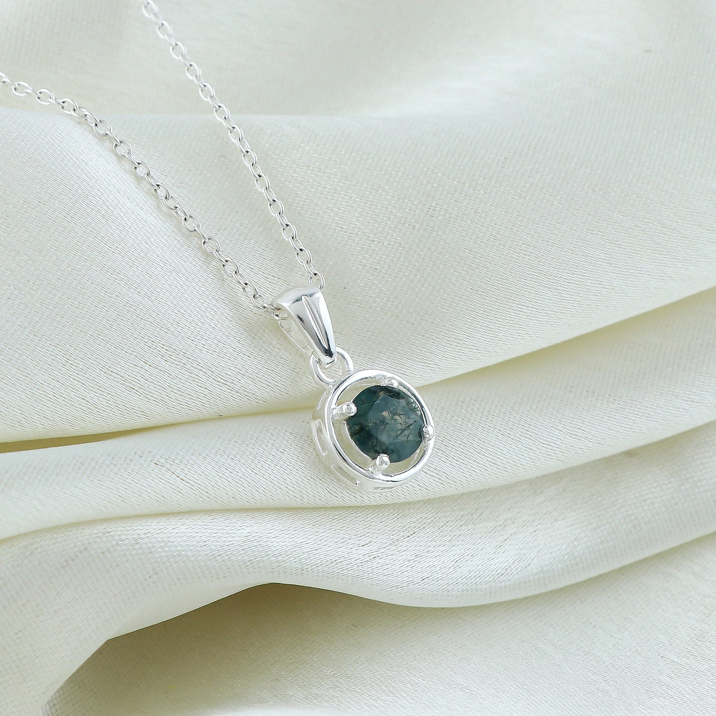 Silver necklace with a green gemstone pendant on a white fabric background