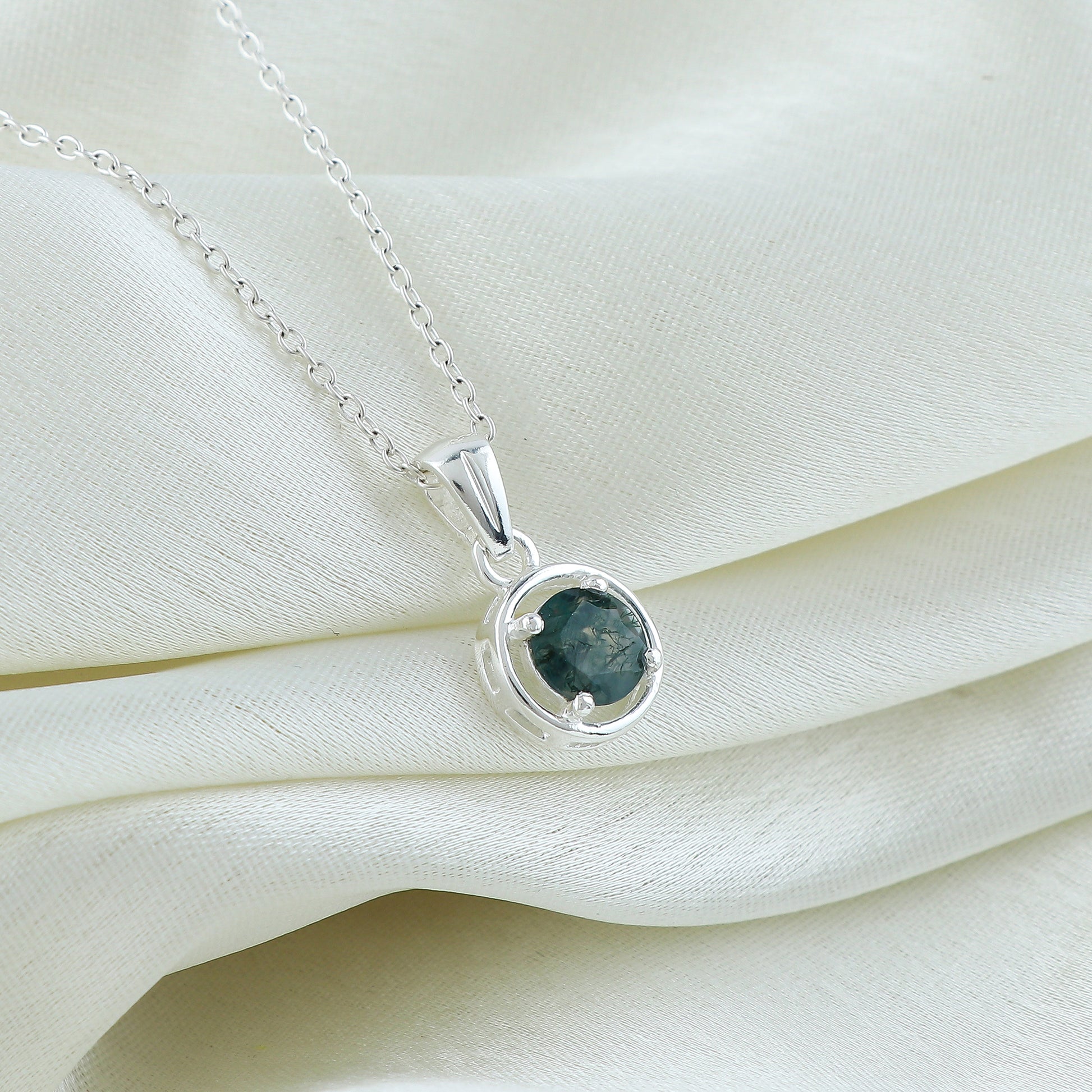 Silver necklace with a green gemstone pendant on a white fabric background