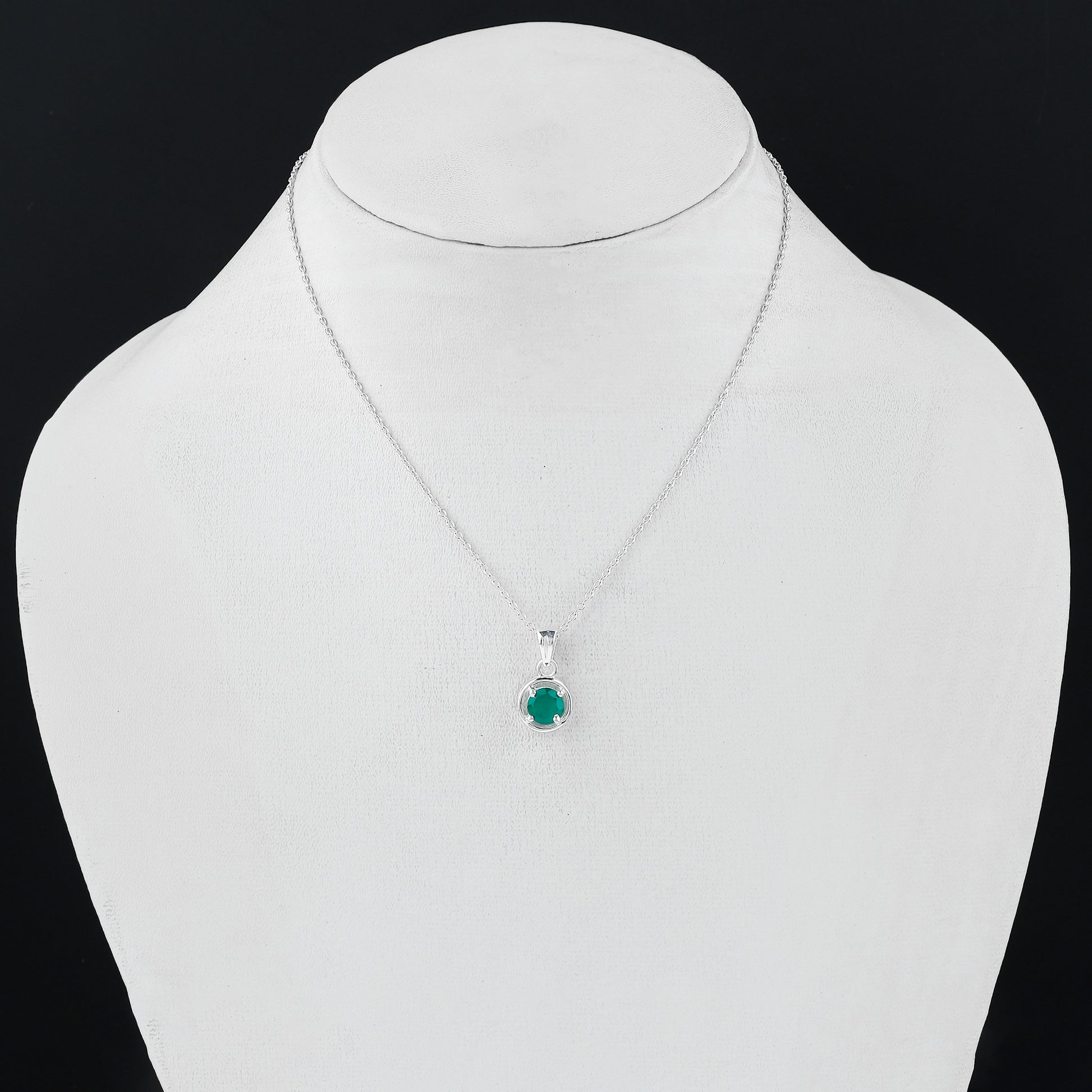 Silver necklace with a green gemstone pendant on a mannequin bust.