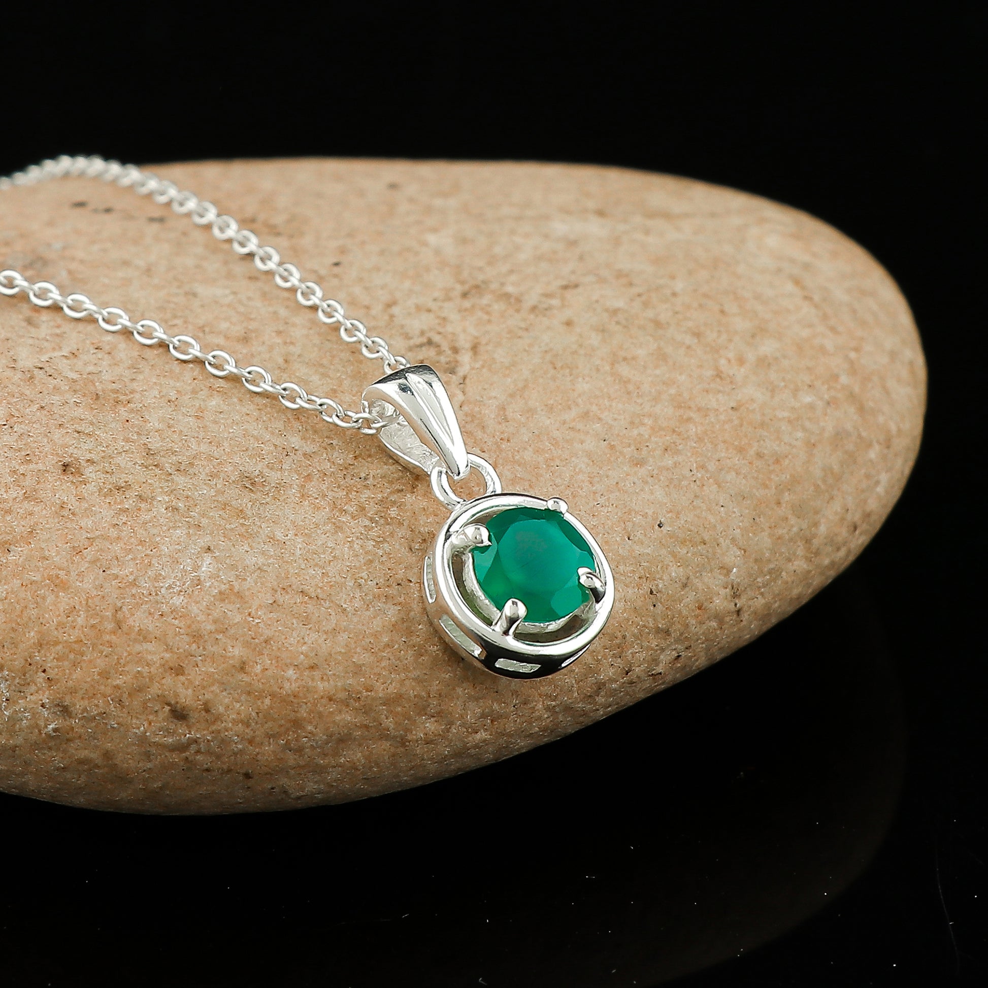 Silver necklace with a green gemstone pendant on a stone surface