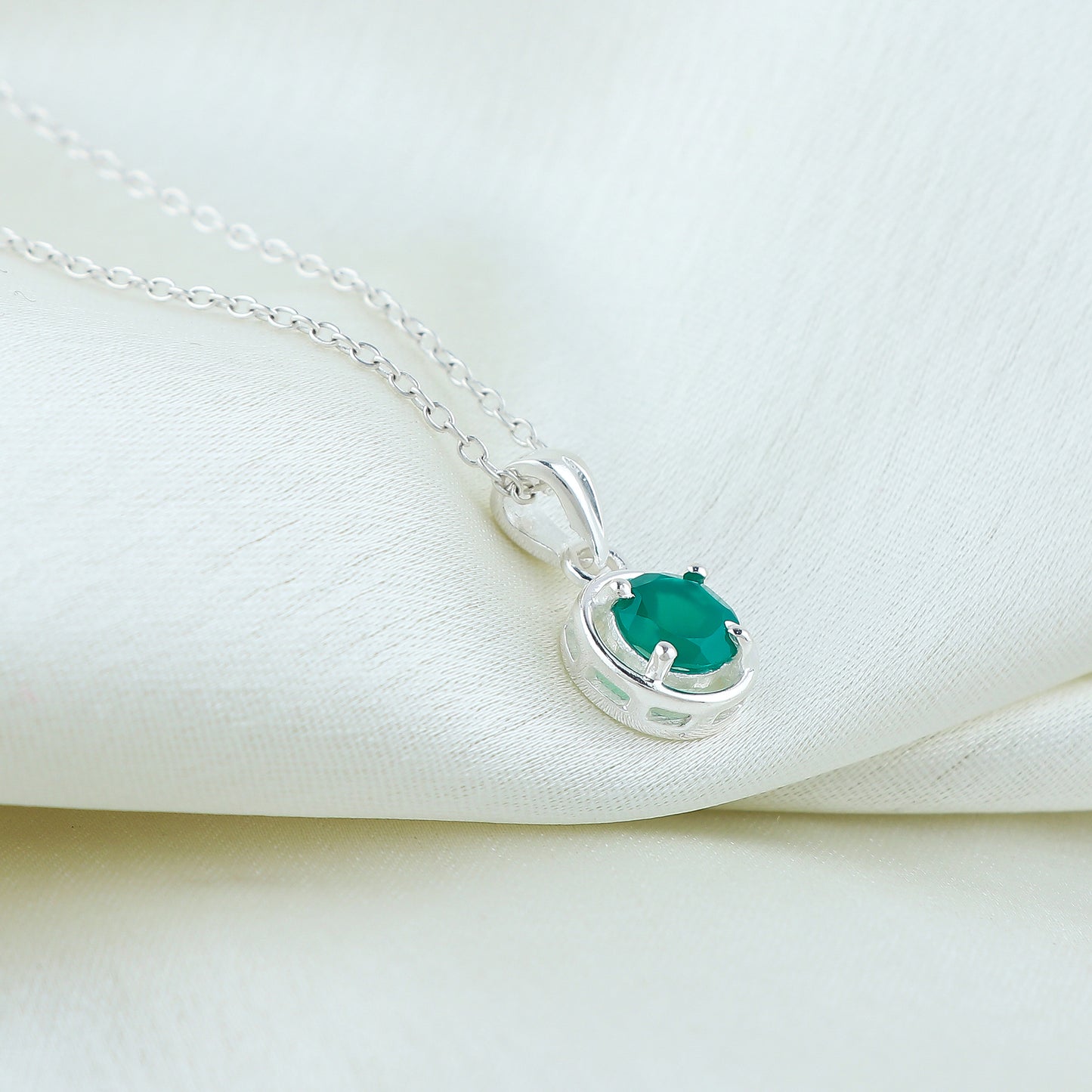 Silver necklace with a green gemstone pendant on a white fabric background