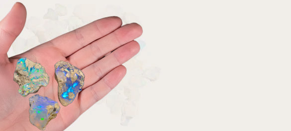 Hand holding three colorful opal stones against a white background