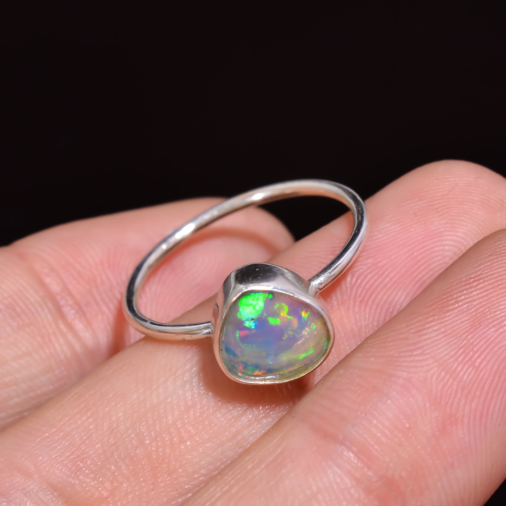 Silver ring with a colorful opal stone on a hand against a dark background
