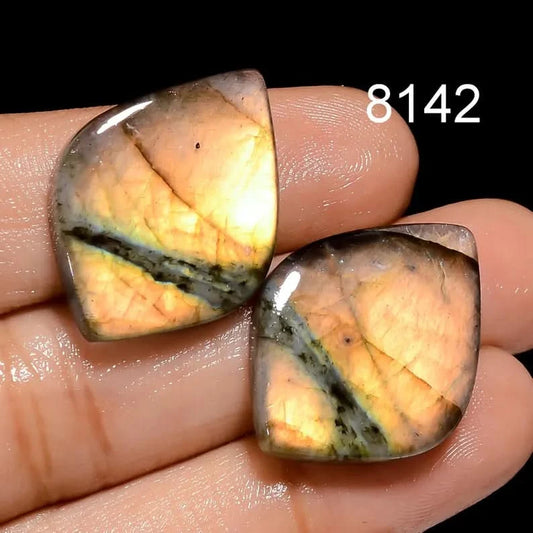 Two cabochon cut gemstones held between fingers with a dark background and number 8142.