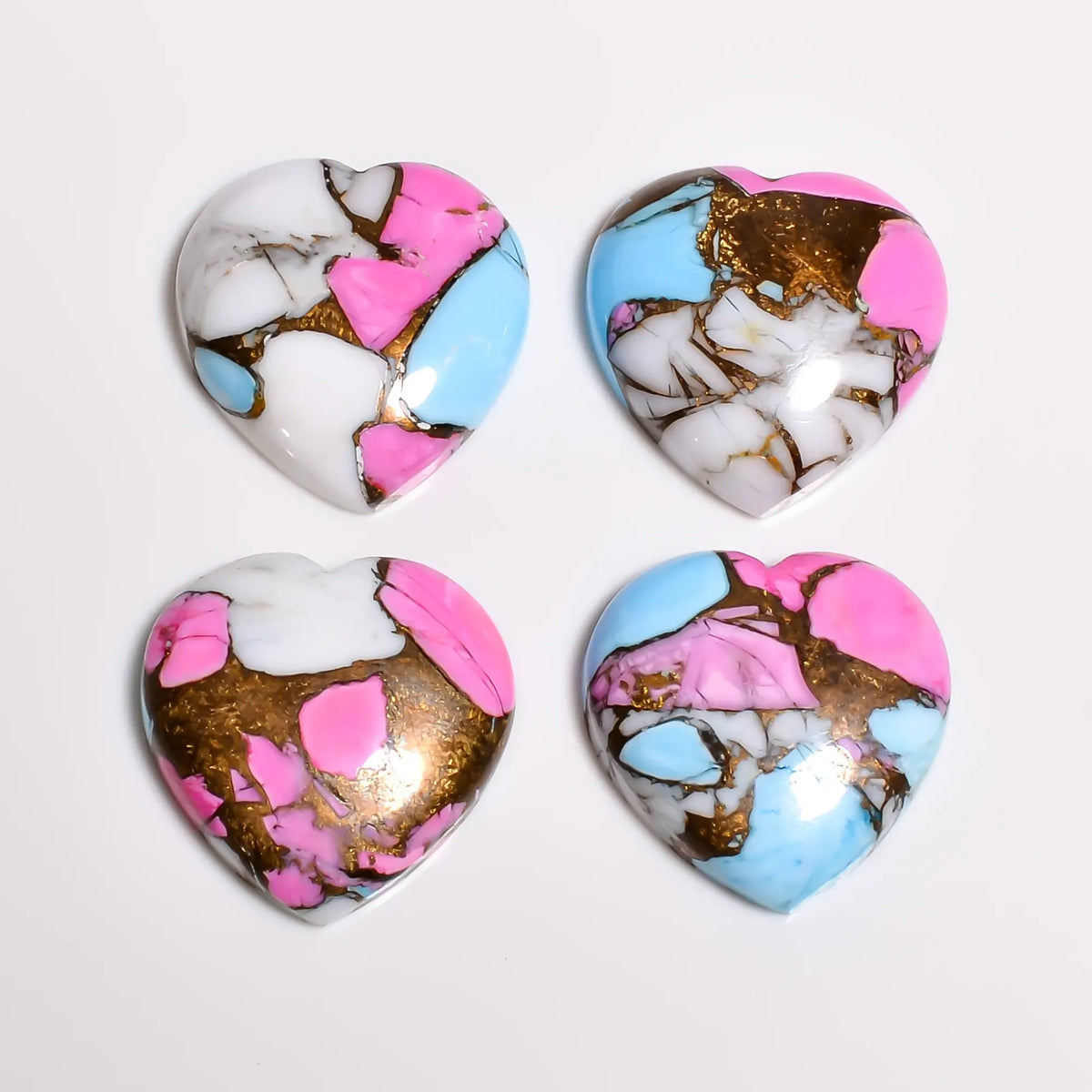 Loose turquoise gemstone hearts in pink, white and light blue with copper matrix, close-up view